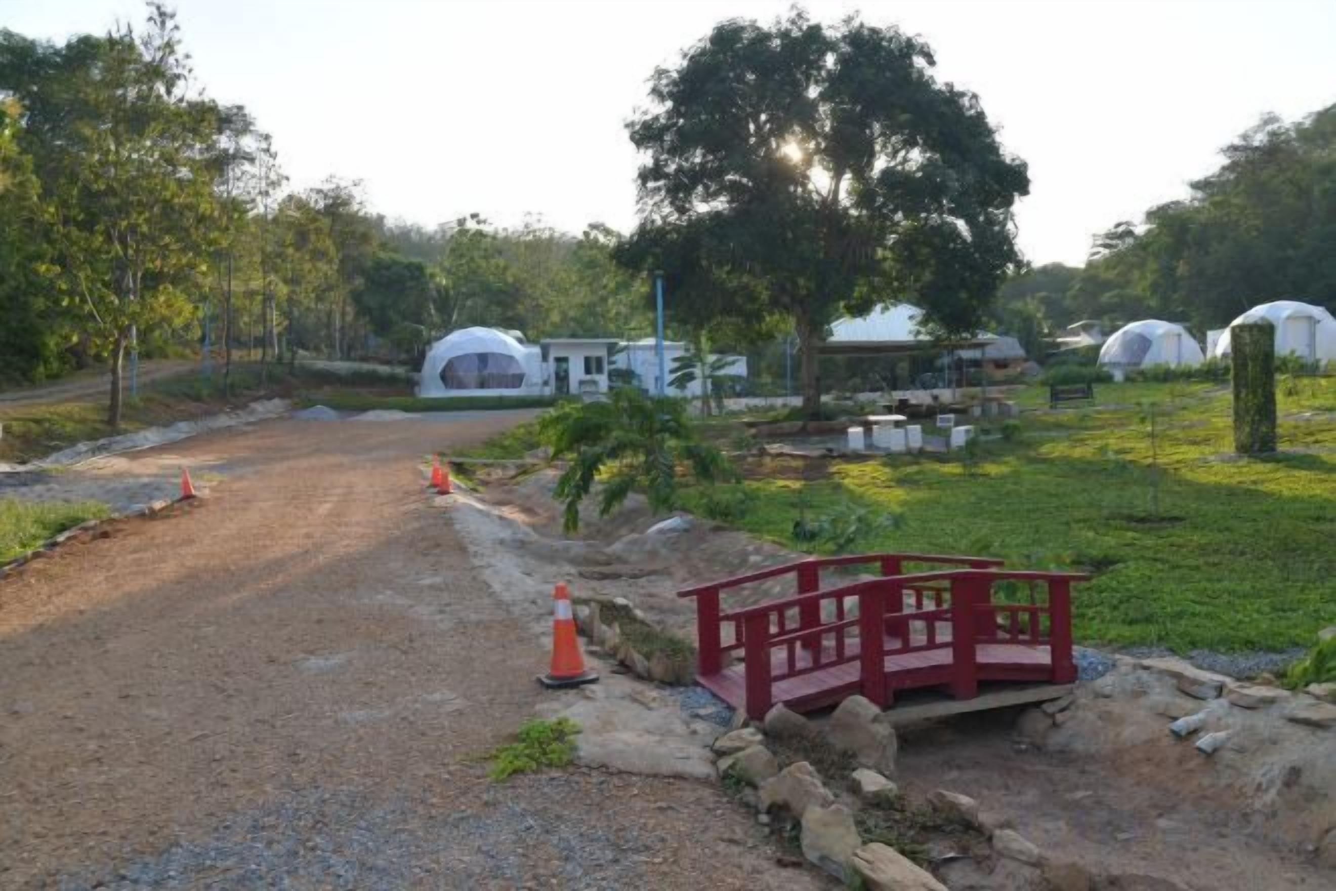 A rural setting with a dirt road, a red bridge, and several white dome-shaped structures.