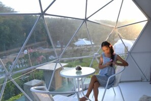Eine Person sitzt in einem Zimmer einer Geodätischen Kuppel mit einem Glastisch und Blick auf eine Landschaft.