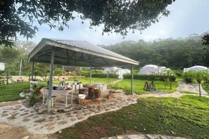 A covered outdoor area with stone flooring, a table with chairs, and a small garden. - NiNo San Glamping - Pak Chong (Pak Chong)