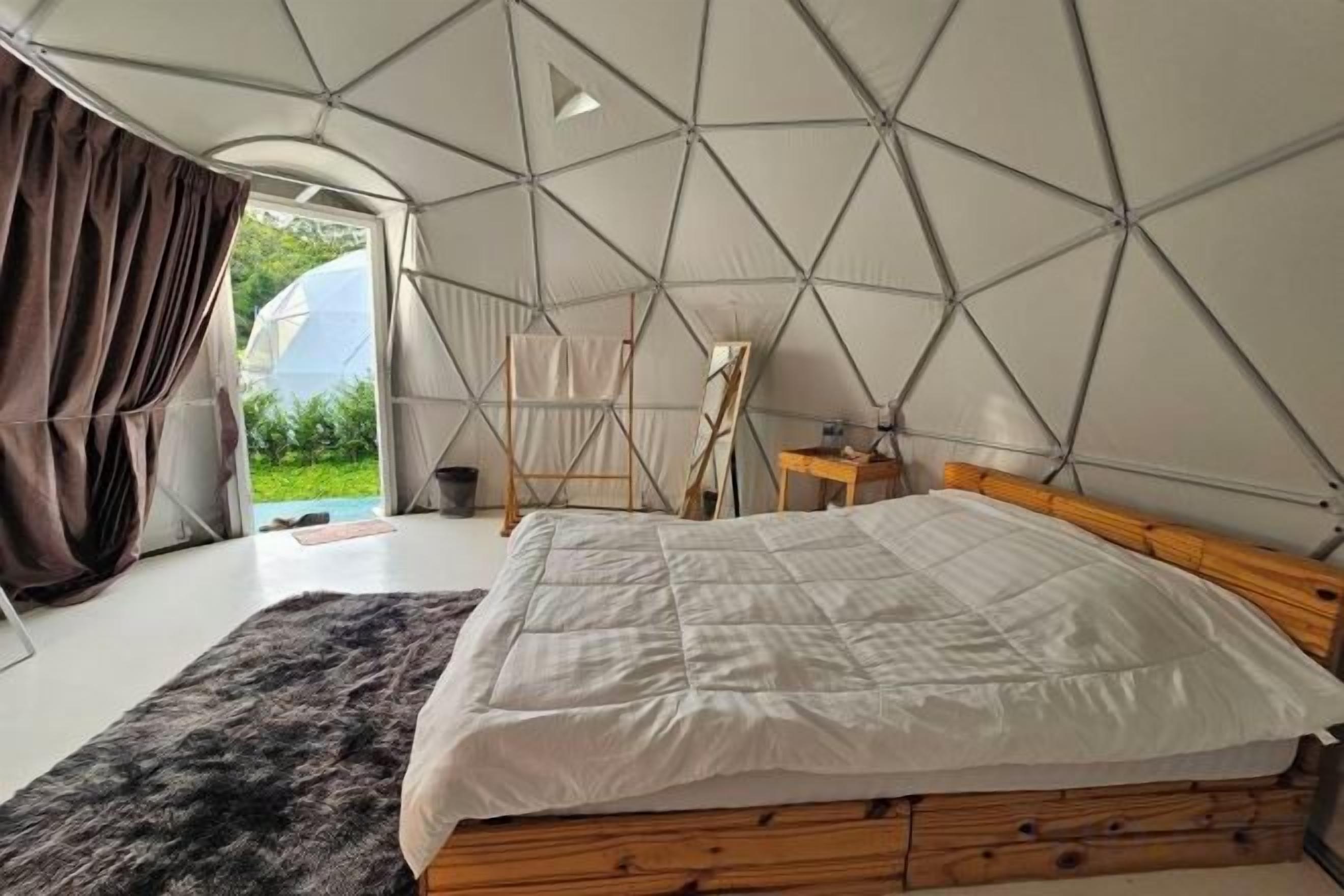 Une chambre aménagée comme une tente, avec un lit, une tête de lit en bois et une vue sur l’extérieur.