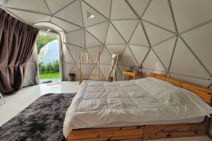 Une chambre aménagée comme une tente, avec un lit, une tête de lit en bois et une vue sur l’extérieur.