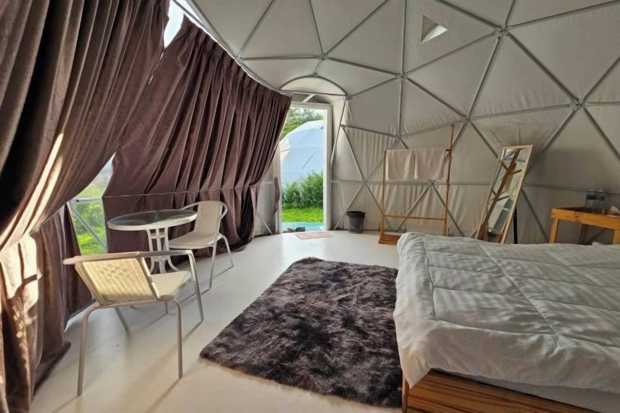 A tented accommodation with a bed, a table, chairs, and a view of the outdoors.