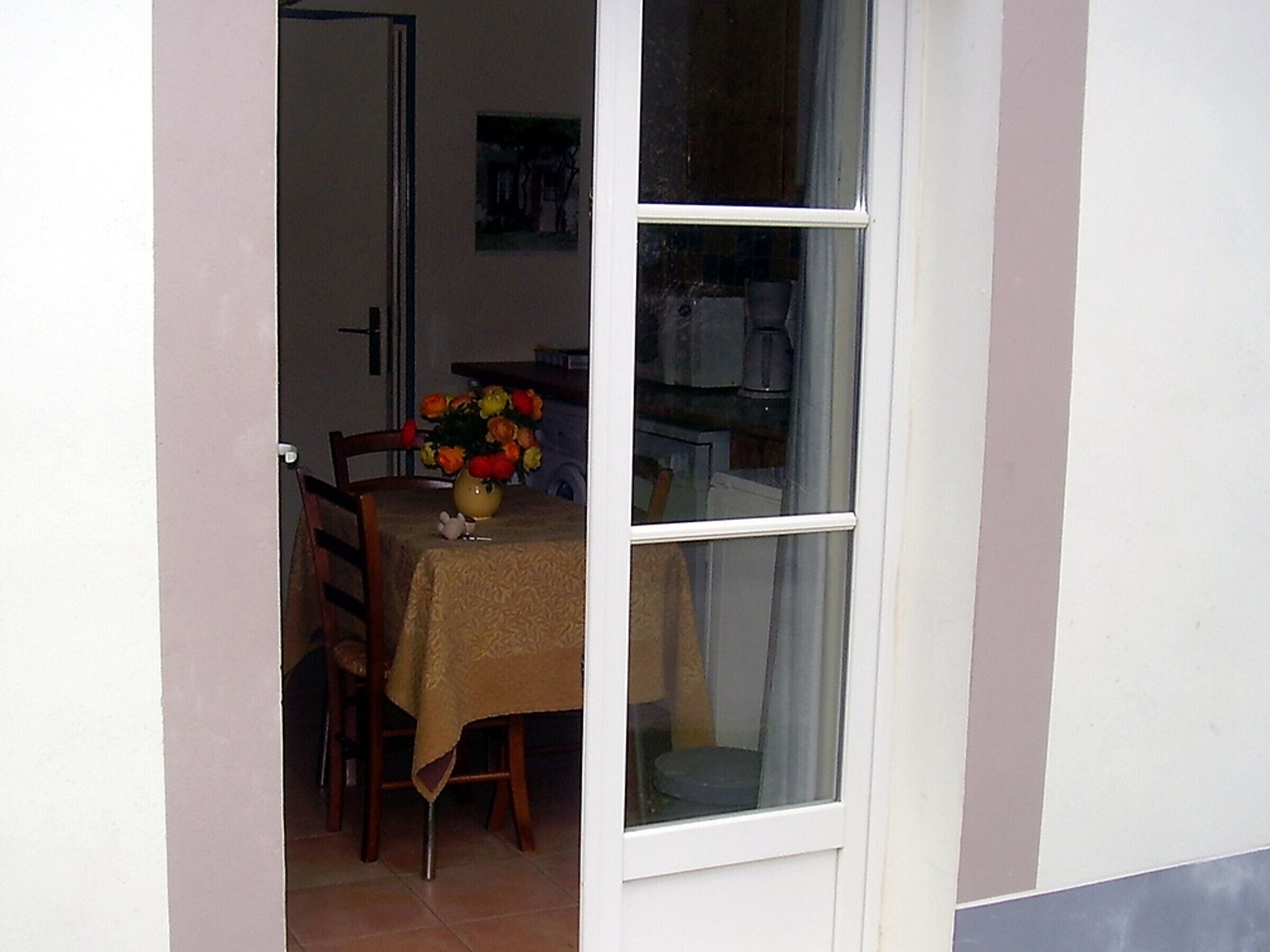 Zona de menjador amb taula per a dues persones, un vas amb flors i una finestra amb cortines.