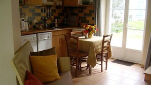 A cozy kitchen with a dining table and chairs, a sofa with cushions, and a window with a view of greenery.