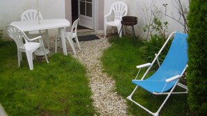 A patio with a white table and chairs, a blue and white striped umbrella, and a blue lawn chair.