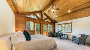 A bedroom with a large bed, a desk, and a chair, wooden ceiling beams, and large windows. - Horizon by Tahoe Getaways - Pet Friendly Tahoe Donner w Hot Tub (Truckee)