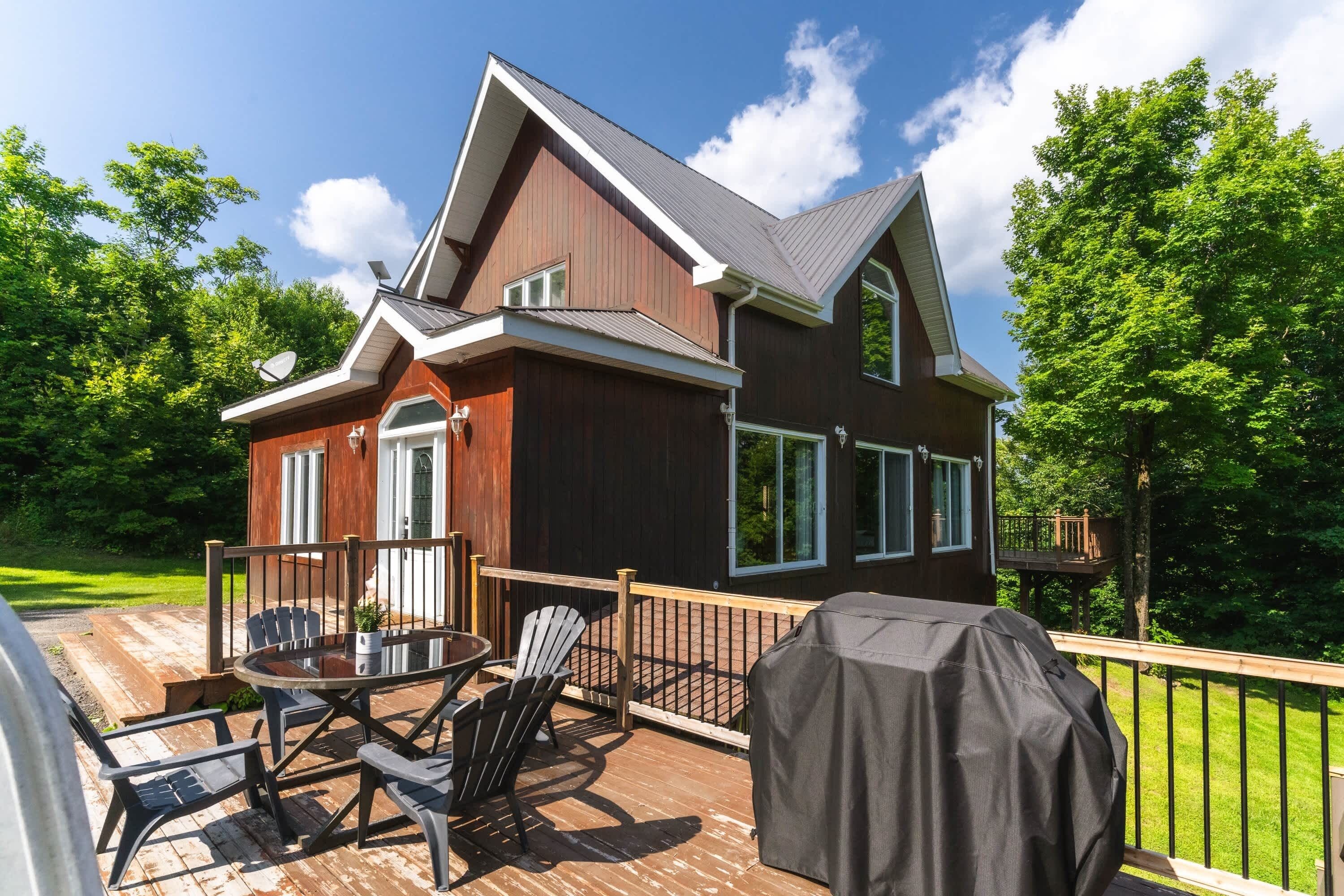 Et træhus med terrasse, grillområde og parabolantenne.