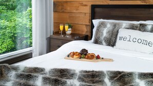 A neatly made bed with a 'welcome' pillow, a wooden nightstand with two glasses of orange juice, and a breakfast tray with croissants and berries. - Cozy chalet with Pool and Spa (Grenville-sur-la-Rouge)