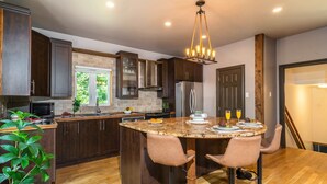 A modern kitchen with dark wood cabinets, a granite countertop, and a central island with bar stools. - Cozy chalet with Pool and Spa (Grenville-sur-la-Rouge)