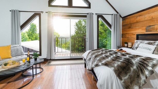 A bedroom with a large bed, a sofa, a small table with drinks, and a balcony with curtains. - Cozy chalet with Pool and Spa (Grenville-sur-la-Rouge)