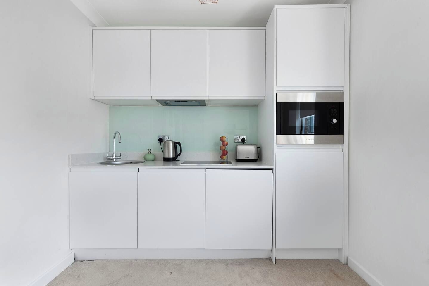 A modern kitchen with white cabinets, a stainless steel range hood, a built-in oven, and a microwave.