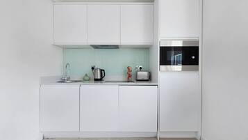 A modern kitchen with white cabinets, a stainless steel range hood, a built-in oven, and a microwave.