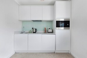 A modern kitchen with white cabinets, a stainless steel range hood, a built-in oven, and a microwave.