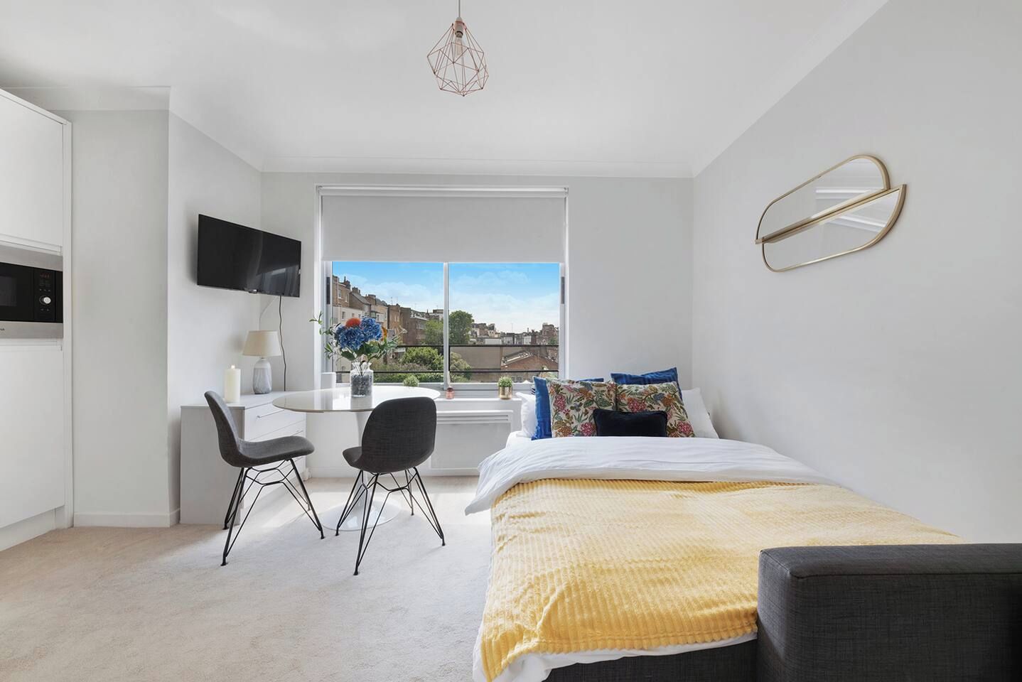 Une chambre moderne comprenant un lit, un bureau, deux chaises, un téléviseur et une fenêtre donnant sur la ville.