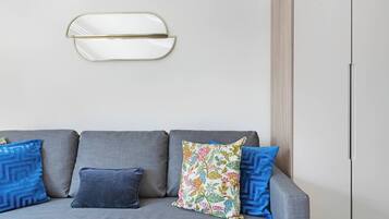A grey sofa with three pillows, one floral and two blue, against a plain wall with a white door and a light switch.
