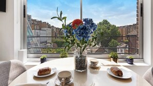 A dining table with a vase of flowers, plates with pastries, and a cup, set against a window overlooking a cityscape.