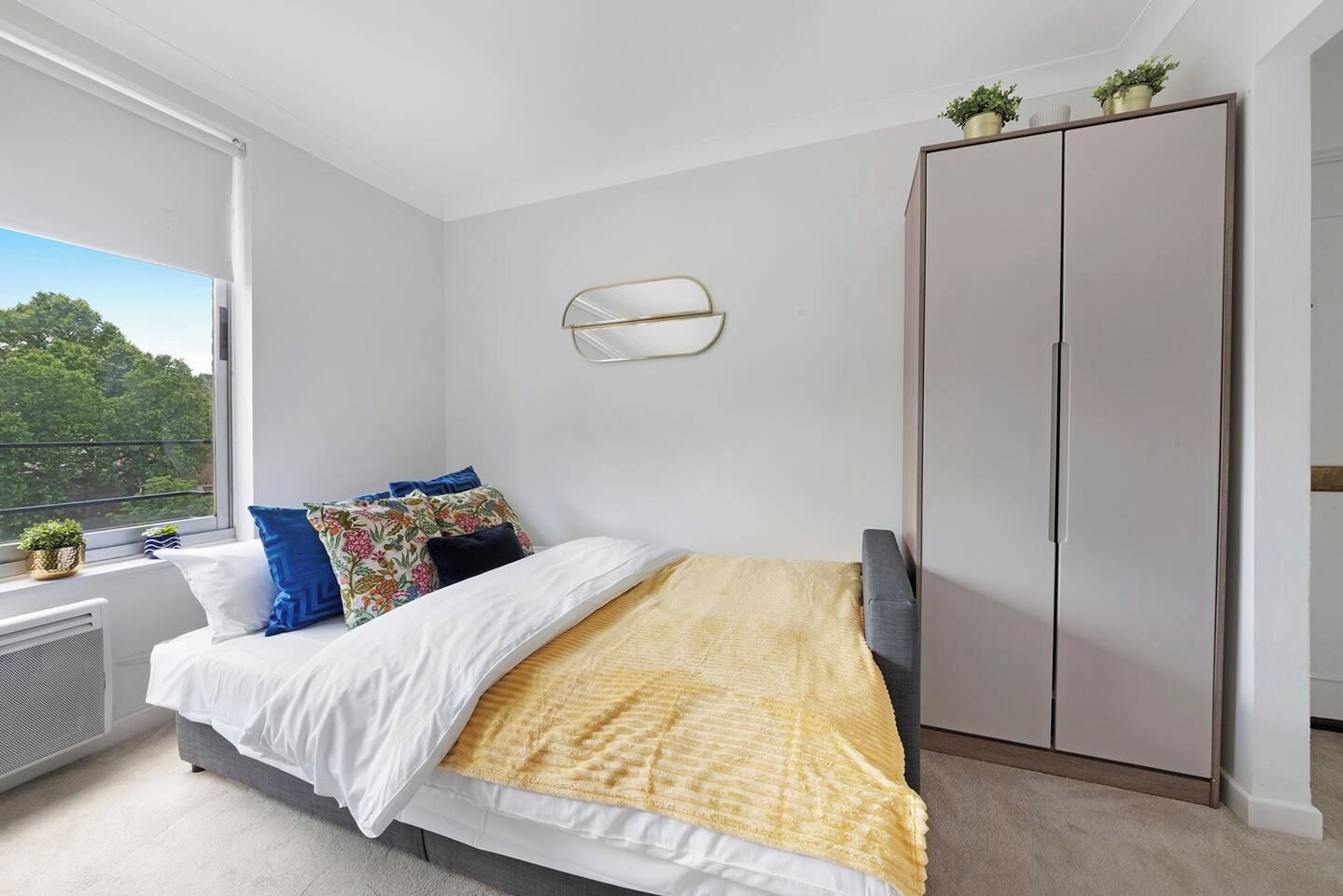 A bedroom with a bed, a wardrobe, a radiator, and a window with a view of trees.
