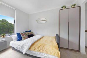 A bedroom with a bed, a wardrobe, a radiator, and a window with a view of trees.