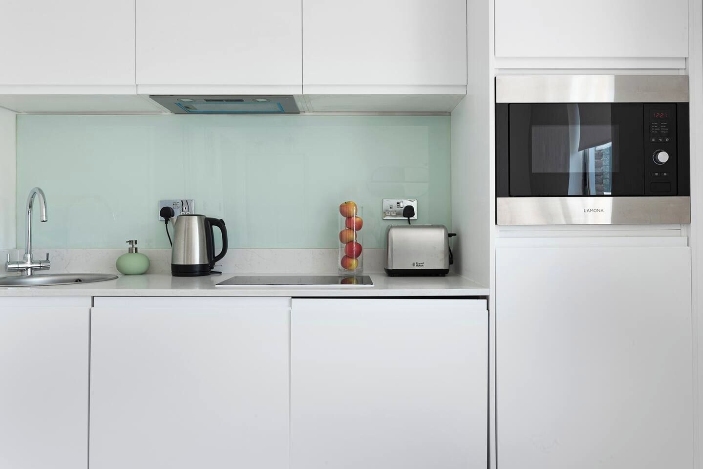 Eine moderne Küche mit Mikrowelle aus Edelstahl, einem Wasserkocher und einem Toaster auf der Arbeitsfläche.