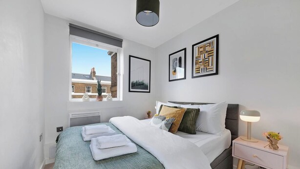 A modern bedroom with a bed, bedside table, lamp, and artwork.