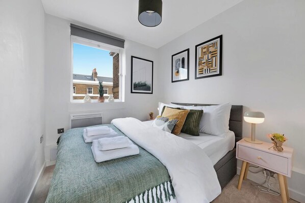 A modern bedroom with a bed, bedside table, lamp, and artwork.