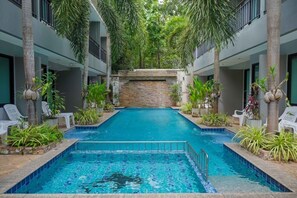 A swimming pool with a stone wall in the center, surrounded by potted plants and white lounge chairs. - XAYA Pool Access Resort - Phuket (Chalong)