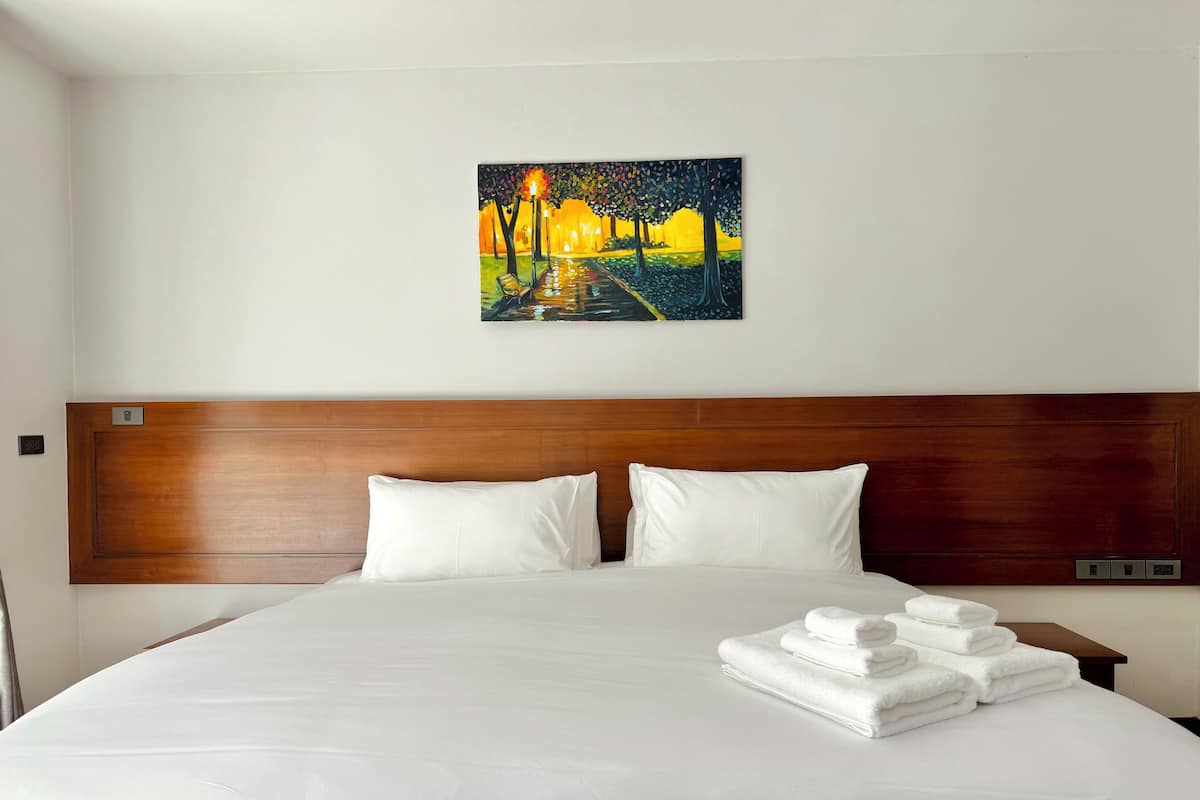 A hotel room with a large bed, white bedding, a wooden headboard, and a painting of a night scene on the wall.