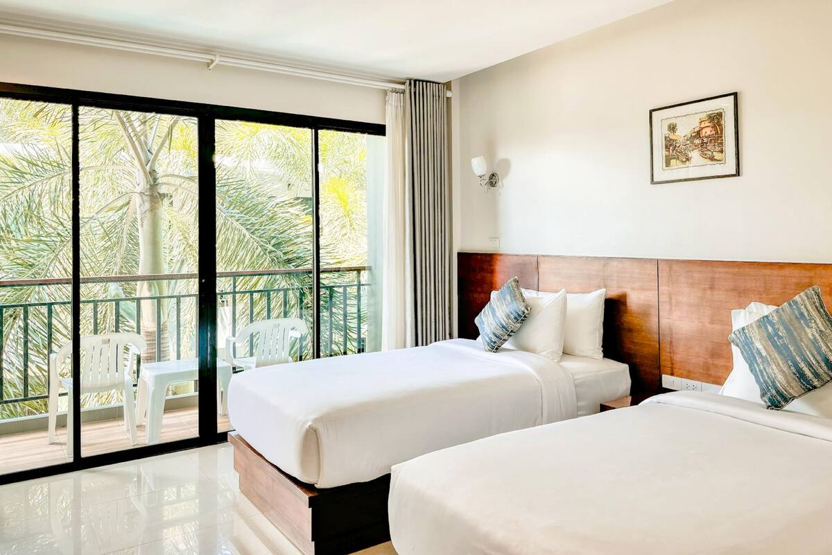 A hotel room with two beds, a balcony with chairs, and a large window with curtains.