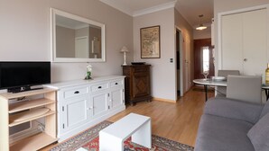 A living room with a flat-screen TV, white entertainment unit, grey sofa, and a patterned rug.
