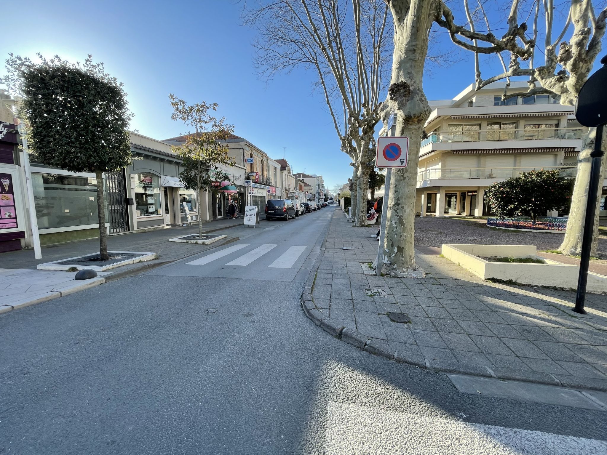 A street view with a pedestrian crossing, storefronts, and a no parking sign.