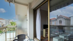 A balcony with a table set for two, a chair, and a view of a building with a red roof.