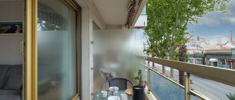 A balcony with a table set for two, a sofa, and a view of the street and buildings.