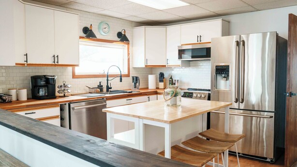 Une cuisine moderne avec des armoires blanches, des appareils en acier inoxydable et un îlot central en bois doté de tabourets de bar.