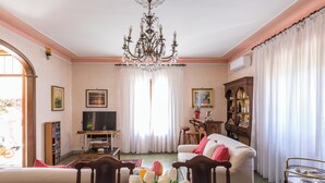 Una sala de estar con candelabro, televisor, sofá y mesa de comedor con tulipanes.