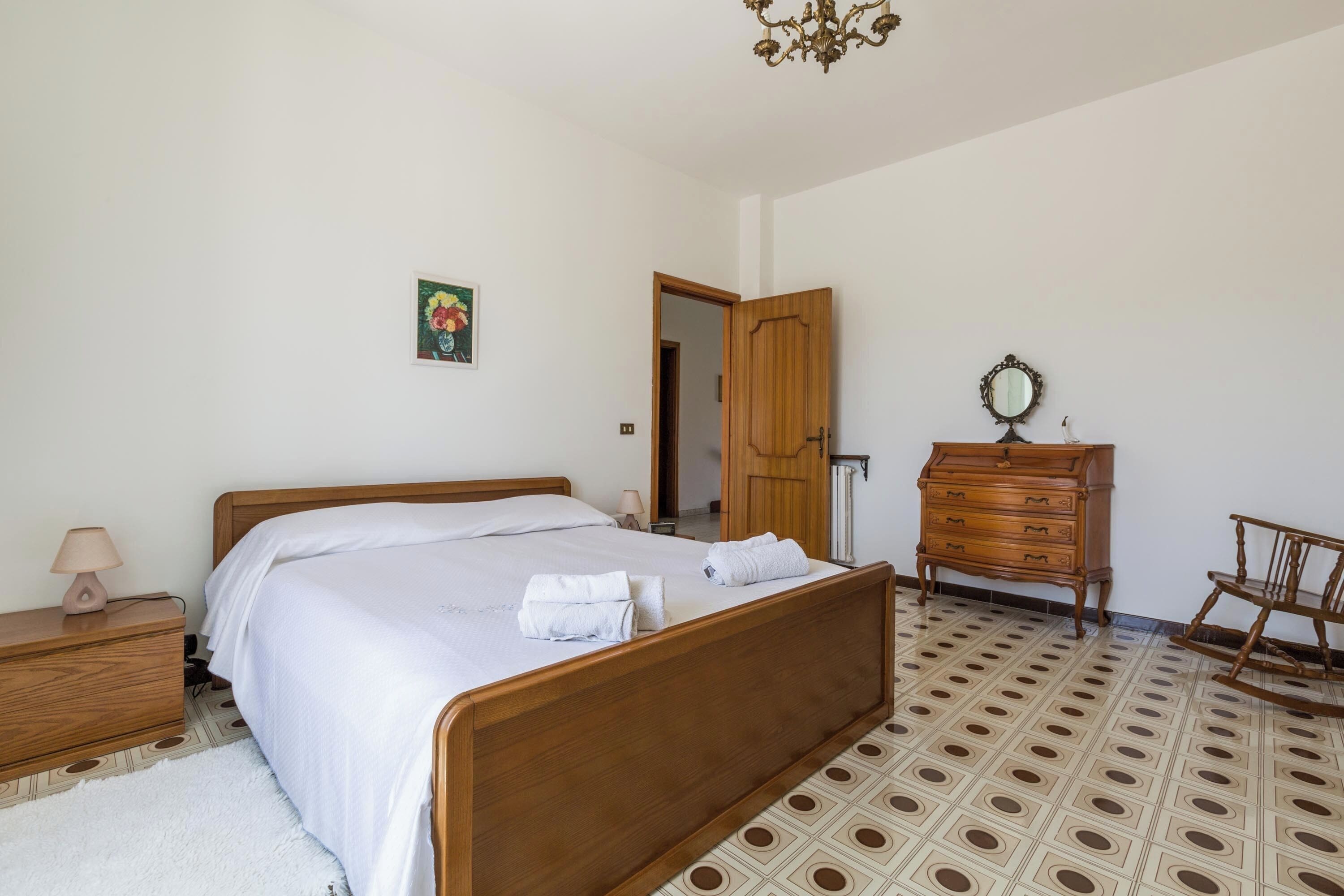 A bedroom with a wooden bed, a dresser, a chair, a mirror, and a patterned floor.