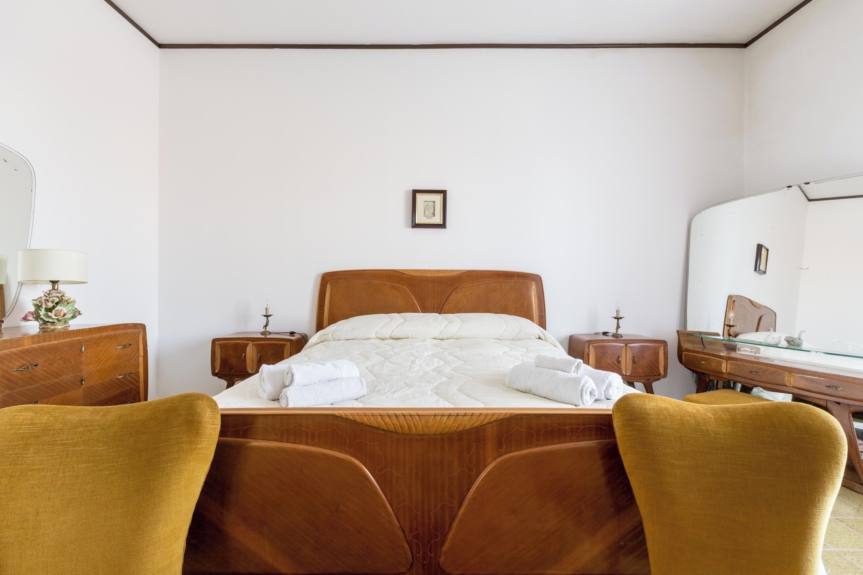 A neatly arranged bedroom with a wooden bed, two bedside tables, a mirror, and a wooden dresser.