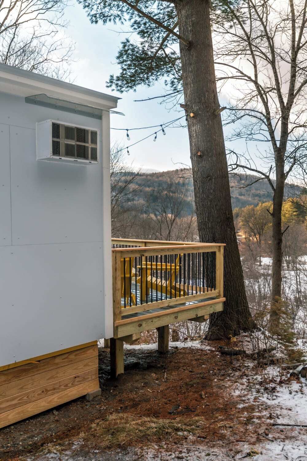 Une petite cabane dotée d’une terrasse en bois et d’un climatiseur en métal.