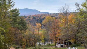 A cabin with a deck and outdoor seating, surrounded by autumn foliage and a mountain in the background.