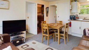 A compact living space with a television, a dining table with chairs, a sofa, and a kitchenette. - Two Bedroom Chalet, in Penstowe Park Near Bude Cornwall close to Beaches. (Kilkhampton)
