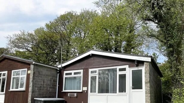 A two-story house with a stone facade, a front porch, and a small garden area. - Two Bedroom Chalet, in Penstowe Park Near Bude Cornwall close to Beaches. (Kilkhampton)