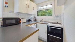 A compact kitchen with white cabinets, a microwave, a kettle, a sink, and an oven. - Two Bedroom Chalet, in Penstowe Park Near Bude Cornwall close to Beaches. (Kilkhampton)