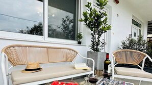 A modern outdoor seating area with wicker furniture, a glass-top table with a bowl of fruit, and a bottle of wine. - Mylos home (Ierapetra)