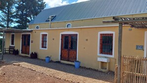 A yellow building with red doors and windows, a metal roof, and a wooden fence. - Gecko Pet-friendly cottage on Fynbos Garden Retreat (Franschhoek)