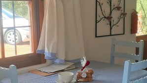 A dining table with a checkered tablecloth, white chairs, a cup, a plate, and a small basket of bread. - Gecko Pet-friendly cottage on Fynbos Garden Retreat (Franschhoek)