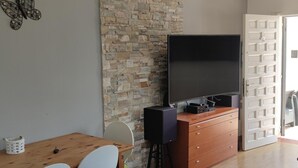 A room with a stone wall, a flat-screen TV on a wooden cabinet, a dining table with chairs, and a white door.