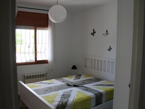 A bedroom with a bed, a radiator, a window with curtains, a hanging light fixture, and wall decorations.