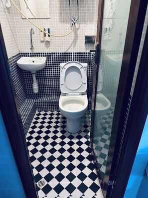 Et badeværelse med gulv i sort og hvid tern, et toilet, en håndvask og en bruseplads.