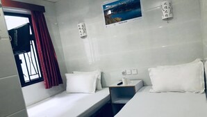 Una habitación de hotel con dos camas, una mesita y un ventanal con cortinas rojas.