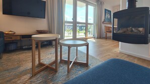 Una sala de estar con televisor, dos taburetes, una chimenea y un ventanal grande.