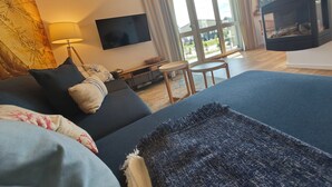 Habitación de hotel moderna con una cama grande, un televisor de pantalla plana, una chimenea y vistas al exterior a través de amplios ventanales.